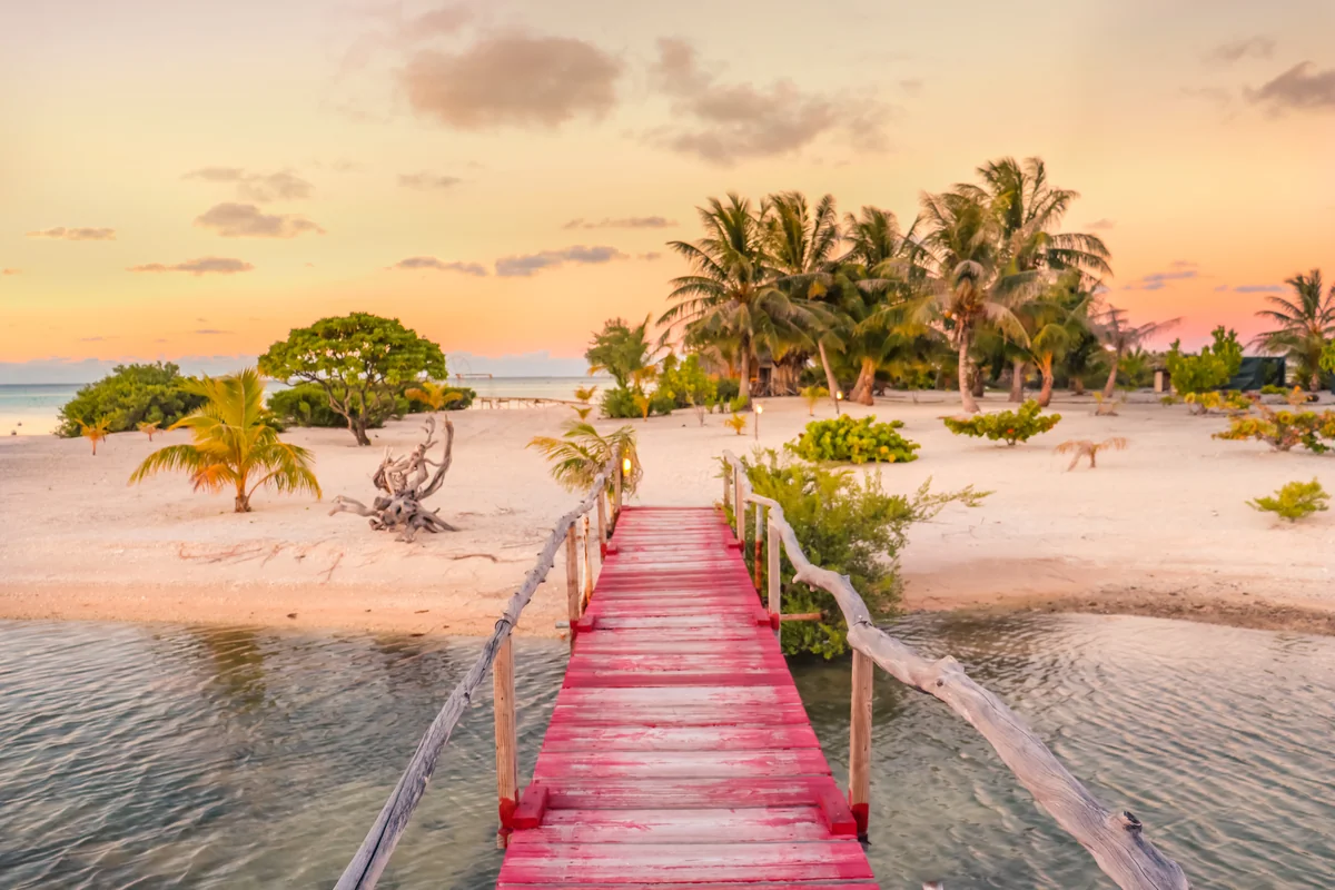 Red wooden jetty leading to a palm-fringed Tikehau beach in warm sunset light